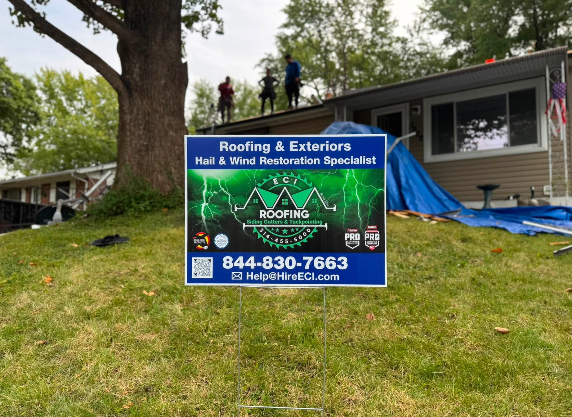 ECI hail and wind restoration yard sign with the crew working the roof behind