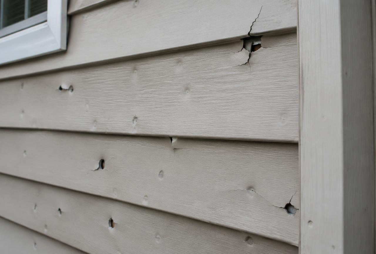 Close-up of vinyl siding cracked and punctured by hail